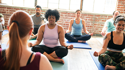 Group sitting in yoga pose in an indoor classroom. 