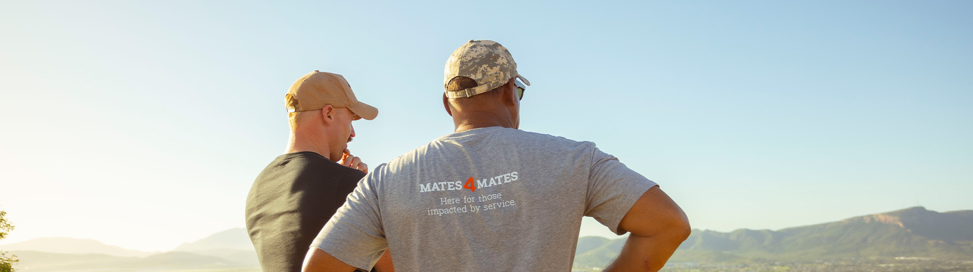 Two men standing together, looking out towards the view of a town below them.