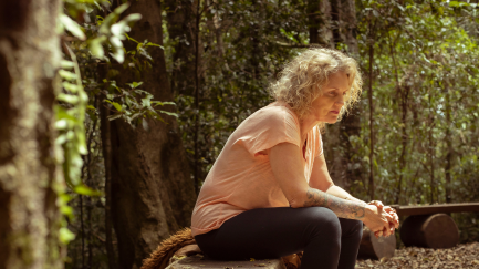 Woman in a forest, sitting on a seat considering her loss