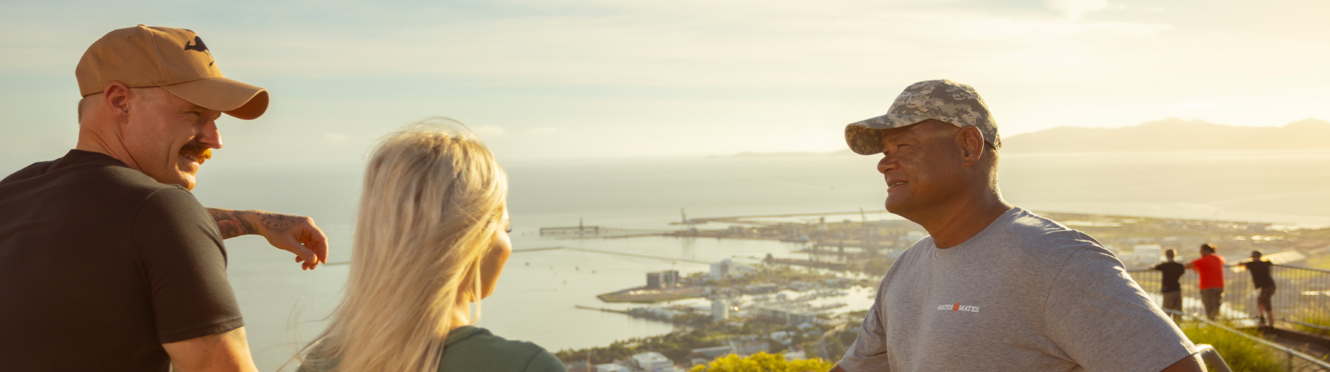 A group of three stopped at a lookout talking together with a view of Townsville in the background.