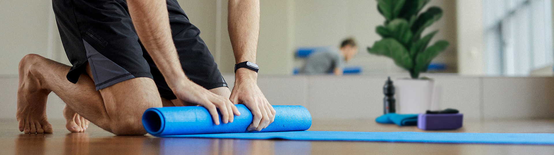 Man wearing Mates4Mates t-shirt rolling out yoga mat in yoga studio