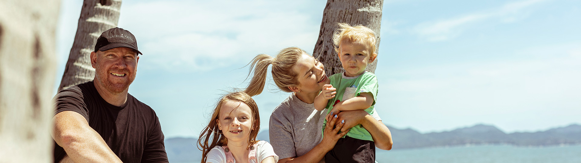 Family of four sitting together under palm trees