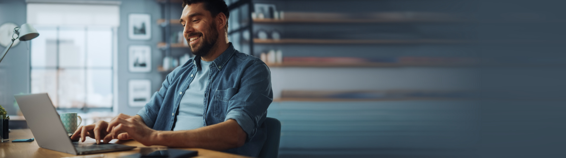 Person sitting in front of a laptop while sitting at a desk, typing and smiling.